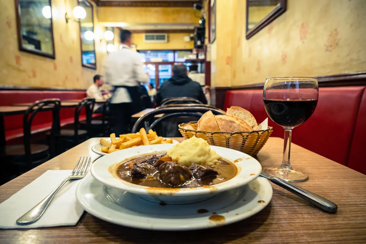 Assiette de bœuf bourguignon, purée, frites, pain, vin rouge dans un restaurant français convivial.