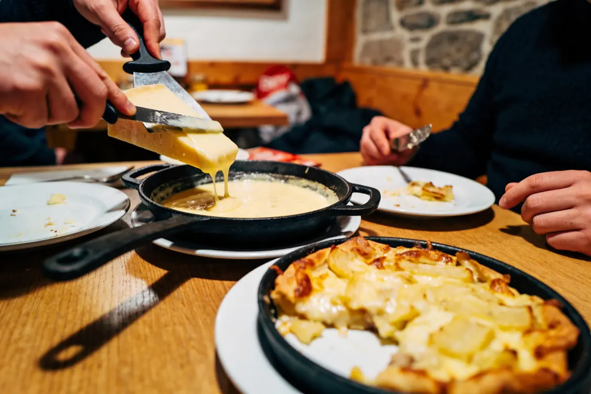 Deux personnes partagent une raclette, fromage fondu et tarte aux pommes de terre, dans un restaurant chaleureux.