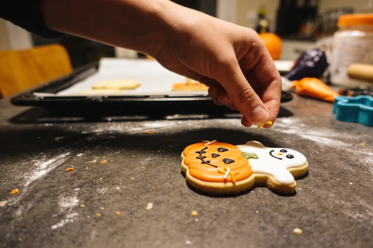 Main décorant biscuit d'Halloween en forme de citrouille et fantôme, sur table de cuisine.