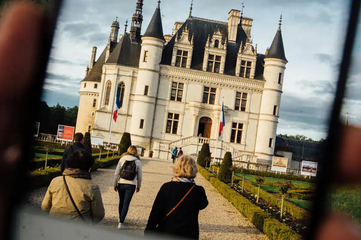 Des touristes marchent vers un château français en arrière-plan, sous un ciel nuageux.